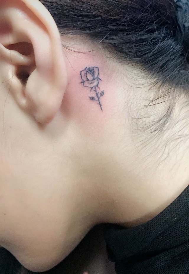 A Woman With A Black Rose Tattoo On Her Ear And Behind The Ear Is A Chain