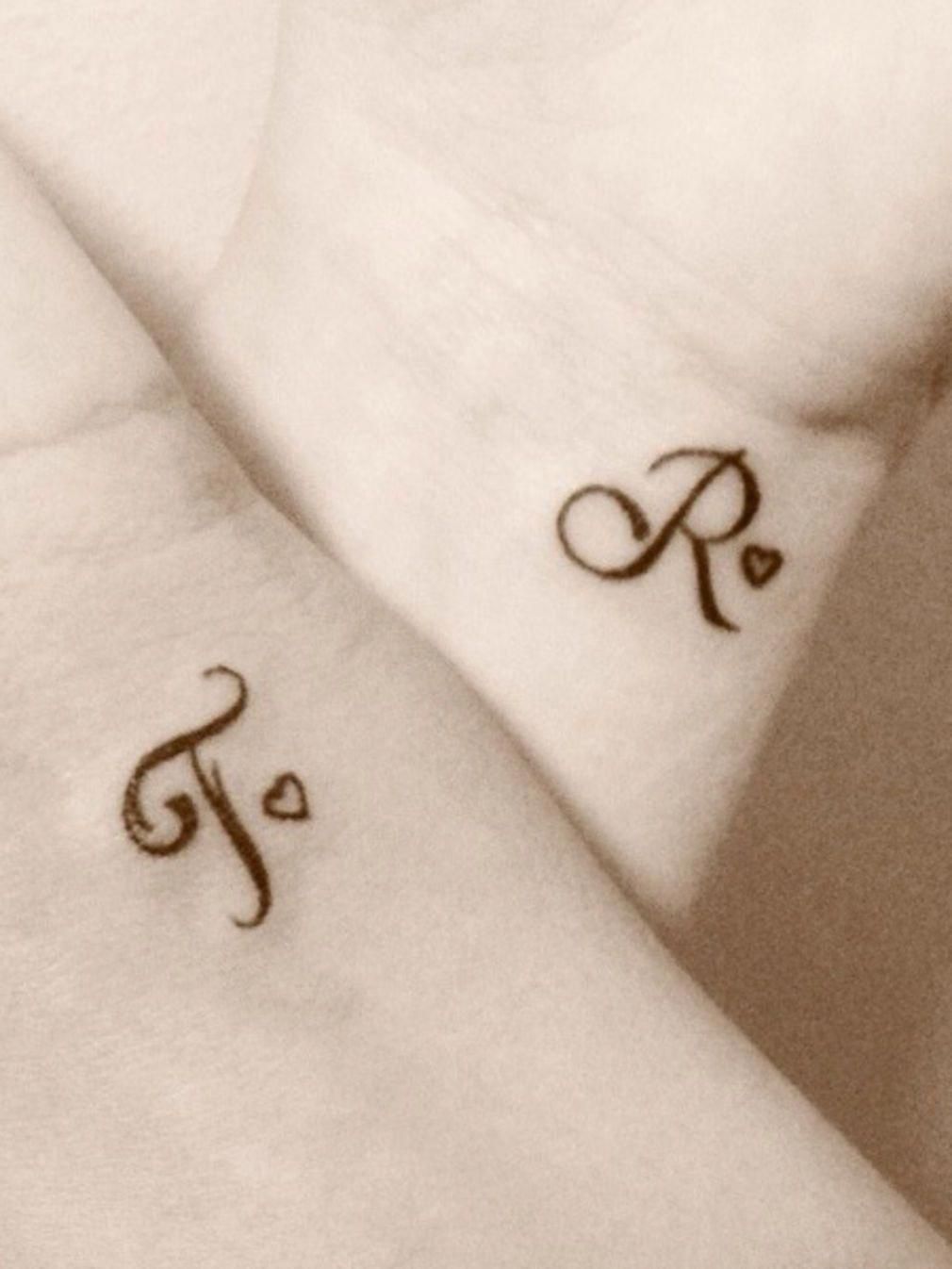 A Wrist Tattoo With The Letter T And Two Wings On It In Front Of A